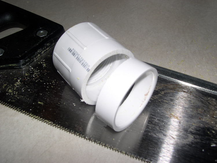 Photograph of coupling after cut, with cut piece, showing handsaw used for the purpose.