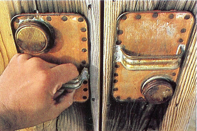 Two gallon solvent can lids cut off and nailed to wooden double doors as improvised pulls.