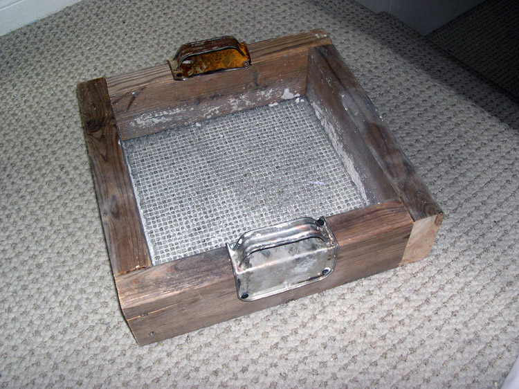 Homemade sand 'riddle' (screen) featuring recycled solvent can handles bent around the frame members and secured with screws.